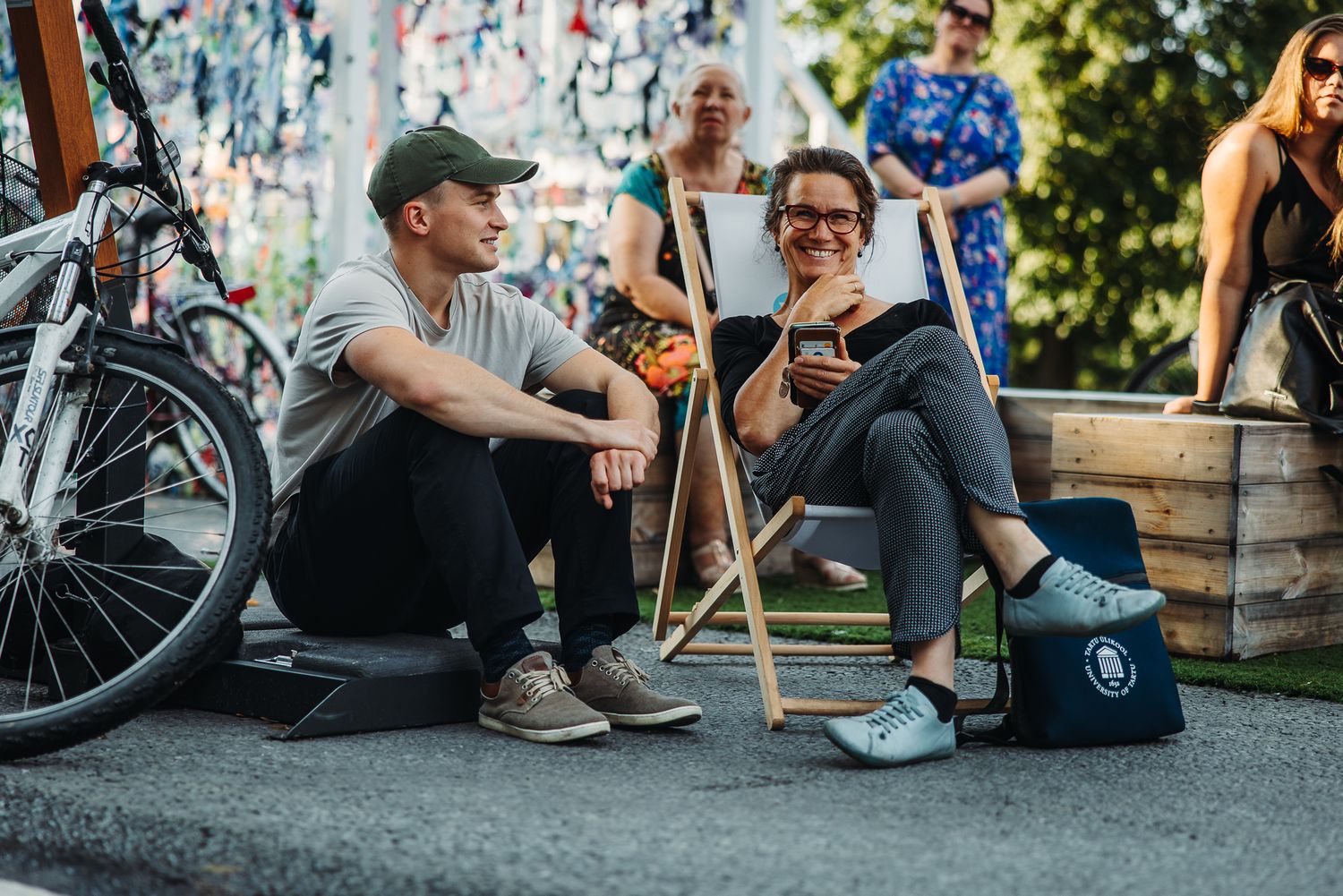 People relaxing and chatting outdoors in Tartu, with bicycles and a lively urban background. hoto: Peeter Paaver. LET'S CREATE A BETTER EXPERIENCE OF SETTLING IN